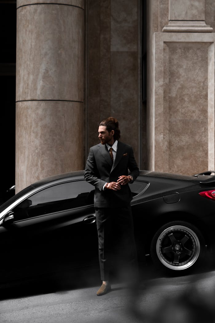 Well-dressed man in formal suit stands by a luxury car on an urban city street.
